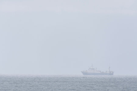 An image of a large fishing vessel barely visible due to a thick mist like haze off the coast of...