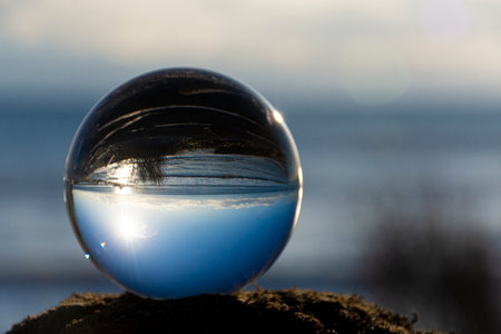 A tranquil image of a glass ball lens reflecting an inverted image of blue sky and the Pacific Ocean.の写真素材