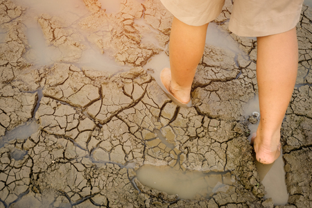 Barefoot on land with dry and cracked ground.  Affected of global warming made climate change. Water shortage and drought concept.の写真素材