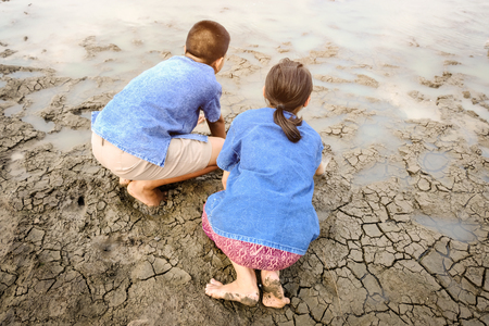 Sad kid despair sitting on cracked earth on The arid lagoon, natural disaster. Affected of global warming made climate change. Water shortage and drought concept.の写真素材