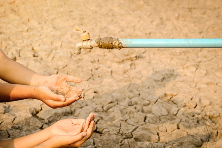 Sad kids sitting on cracked earth open metal water old faucet on hot and dry empty land. Affected of global warming made climate change. Water shortage and drought concept.の写真素材
