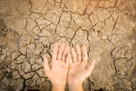 Hands dirty on cracked barren soil background. Affected of global warming made climate change. Water shortage and drought concept.の写真素材