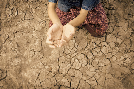 Sad kid despair sitting on cracked earth on hot and dry empty land. Affected of global warming made climate change. Water shortage and drought concept.の写真素材