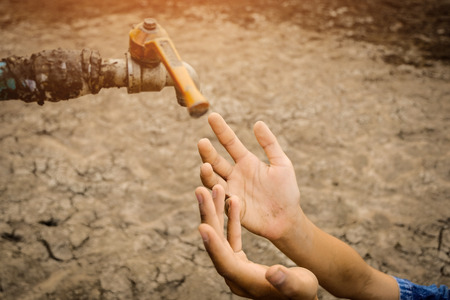 Sad kids sitting on cracked earth open metal water old faucet on hot and dry empty land. Affected of...