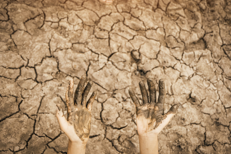 Hands dirty on cracked barren soil background. Affected of global warming made climate change. Water shortage and drought concept.の写真素材