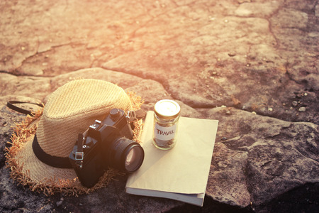 Saving money for vacation concept, glass coins container , Old cameras, hats and a book and nature background.の写真素材