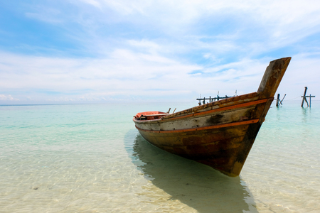 Old wooden boat and blue sea under cloudy sky on white beach in sunny day.の写真素材