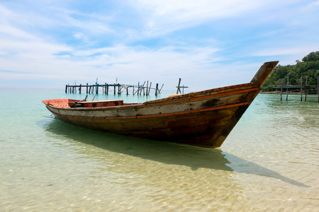Old wooden boat and blue sea under cloudy sky on white beach in sunny day.の写真素材