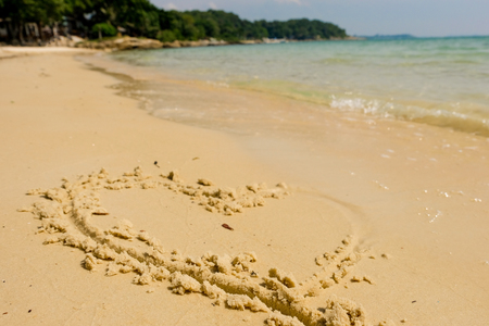 Heart drawn on a sand of beach with the wave of the sea in the bright sunlight, Romantic love background.の写真素材