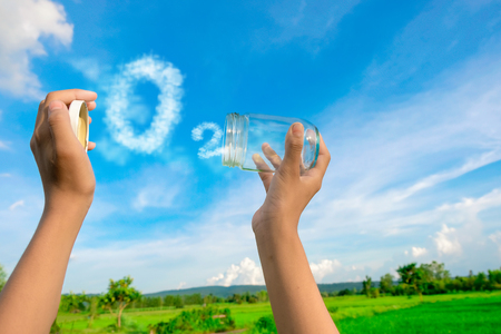 Hands holding glass jar for keeping fresh air, O2 cloud word with a blue sky in the background. concept of clean atmosphere, fresh air and a green environment.の写真素材