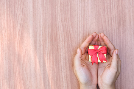 Hands holding a small gift wrapped with red ribbon on wooden table.の写真素材