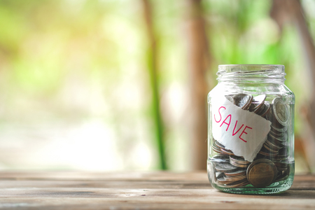 saving money with hand putting coins in jar glass, save and investment money for prepare in the future - saving financial conceptの写真素材