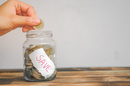 saving money with hand putting coins in jar glass, save and investment money for prepare in the future - saving financial conceptの写真素材