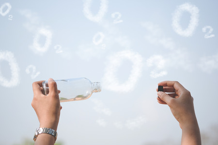 Hands holding glass jar for keeping fresh air, O2 cloud word with a blue sky in the background. concept of clean atmosphere, fresh air and a green environment.の写真素材