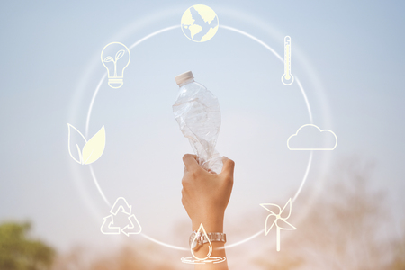 Hand holding plastic bottle on blue sky with icons about environment on image - concept of environmentally friendly with recycling.の写真素材