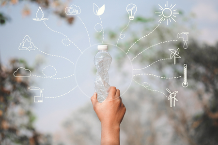 Hand holding plastic bottle on blue sky with icons about environment on image - concept of environmentally friendly with recycling.の写真素材