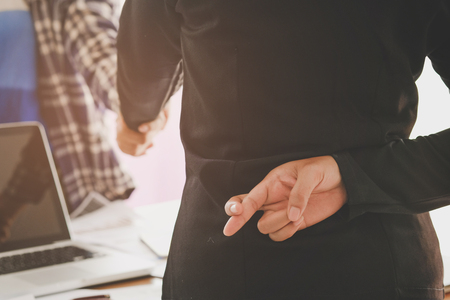 Business people shaking hands and one of them holding fingers crossed behind back, Represents the betrayal.の写真素材