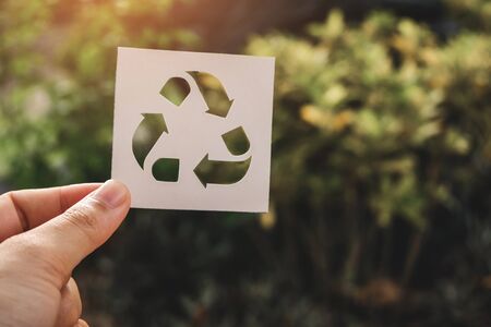 Hand holding recycling symbol created with paper cut and landscape on background, Concept of environmental conservation and protection.の写真素材