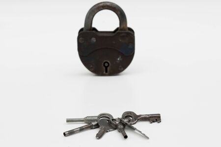 Old rusty padlock and set of six keys closeup against white background. Focus on foreground.の写真素材
