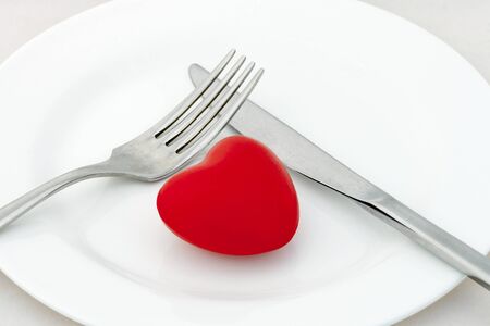 Red heart on plate with fork and knife on white backgroundの写真素材