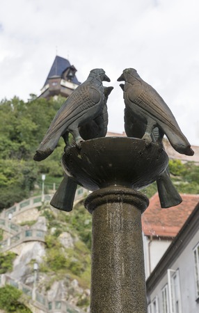 Four dove fountain closeup on Schlossbergplatz and Castle mountain with clock tower in the background. Graz, Styria, Austria.のeditorial素材