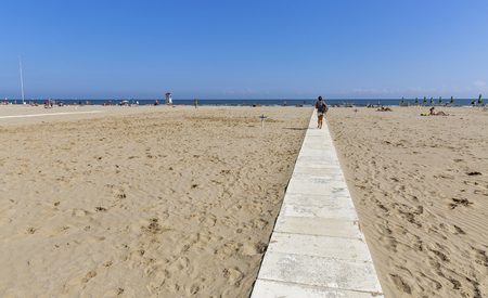 RIMINI, ITALY - SEPTEMBER 25, 2016: Woman walk along walkway through the city sandy beach to the blue sea. Rimini is one of most famous Adriatic Sea resorts in Europe thanks to 15 km long sandy beach.のeditorial素材