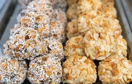 Pile of homemade sweets. Peanuts and coconut balls closeup on market stall outdoors.