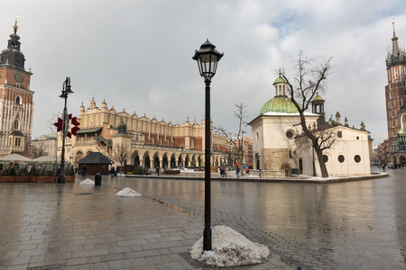 Foto de KRAKOW, POLAND - JANUARY 12, 2017: Unrecognized people walk along Church of St. Wojciech and St. Mary Church on Main Market square in old town. Krakow is one of the oldest cities in Poland. - Imagen libre de derechos