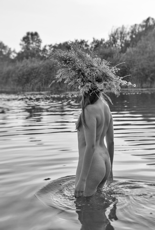 Beautiful caucasian young naked woman with wreath of flowers have fun in water. Ivan Kupala holiday celebration. Black and white.の写真素材
