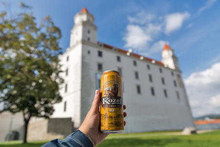 BRATISLAVA, SLOVAKIA - SEPTEMBER 25, 2017: White man's hand holds a can of Velkopopovicky Kozel Czech lager beer closeup with Bratislava medieval Castle in the background.のeditorial素材