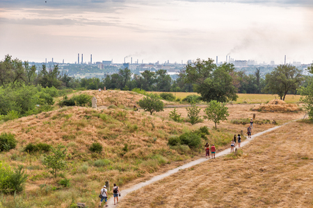 KHORTYTSIA, UKRAINE - JULY 03, 2018: Unrecognized tourists visit ancient Scythian mounds and stone idols of Khortytsia island. Zaporogie industrial city skyline in the background.のeditorial素材