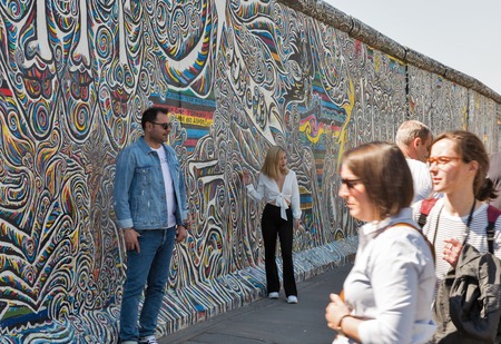 BERLIN, GERMANY - APRIL 18, 2019: People visit Wall barrier and East Side Gallery, international memorial for freedom along Spree river at sunny day.のeditorial素材