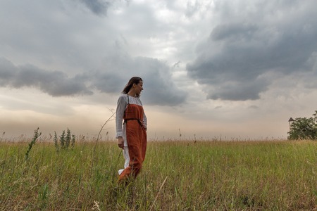 KHORTYTSIA, UKRAINE - JULY 03, 2018: Middle aged white woman in medieval dress walks in the steppe with thunder sky summer landscape on Khortytsia island.のeditorial素材
