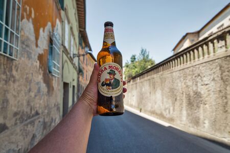 MONTOPOLI, ITALY - JULY 24, 2019: White man's hand holds a Moretti Italian beer, ancient street in background. Montopoli in Val d'Arno is a municipality in the Province of Pisa in the region Tuscany.のeditorial素材