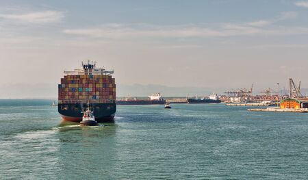 LIVORNO, ITALY - JULY 23, 2019: Tugs and huge cargo container ship Maersk Kowloon entering port....