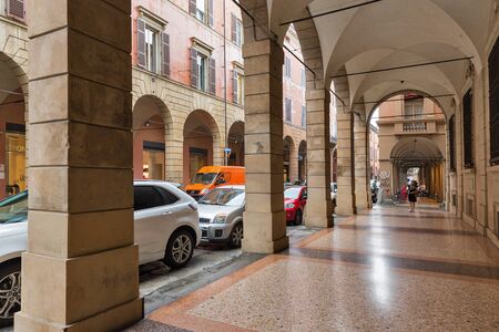 BOLOGNA, ITALY - JULY 10, 2019: People walk along ancient narrow street under rain. Bologna is the...