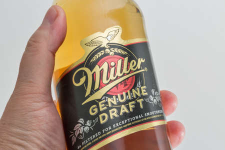 KYIV, UKRAINE - JUNE 17, 2020: Miller Genuine Draft lager beer bottle closeup in human hand against white background. Miller Brewing is an American beer company headquartered in Milwaukee, Wisconsin.のeditorial素材