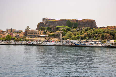 Kerkyra, Corfu, Greece - August 10, 2021: Cityscape with New Fortress and marina sea bay with calm turquoise water and colorful old houses.のeditorial素材