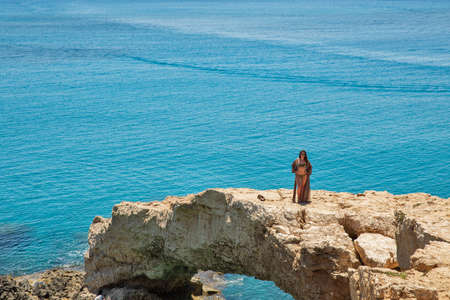 AYIA NAPA, CYPRUS - MAY 24, 2021: Beautiful young woman in bikini standing on rocky coastline arch....