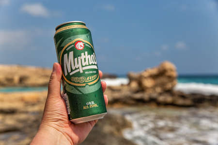 Ayia Napa, Cyprus - May 29, 2021: White man's hand holds a can of Mythos Cypriot beer closeup with...