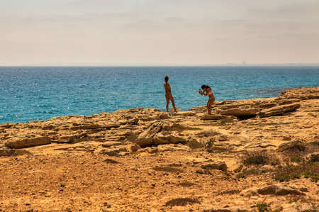 Ayia Napa, Cyprus - May 27, 2021: Young beautiful women make smartphone photos in Cape Greco peninsula park. It is mountainous peninsula with a national park, rock paths and turquoise lagoon.のeditorial素材