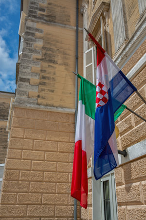 Croatian and Italian flags hanging on the facade of a historic building in Porec, Croatia. European diplomacy, cultural cooperation, international relations, national symbols, travel in Europe.の写真素材