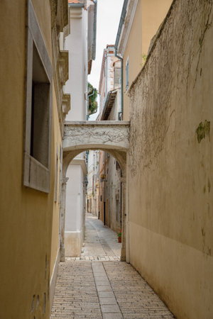 Charming narrow stone alley with archway in a historic European town Porec, Istria, Croatia. Textured walls, old architecture, peaceful street, travel and tourism, authentic Mediterranean vibe.の写真素材