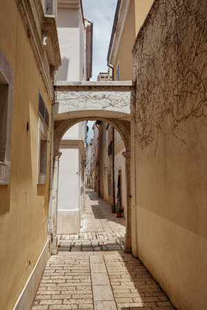 Charming narrow stone alley with archway in a historic European town Porec, Istria, Croatia. Textured walls, old architecture, peaceful street, travel and tourism, authentic Mediterranean vibe.の写真素材