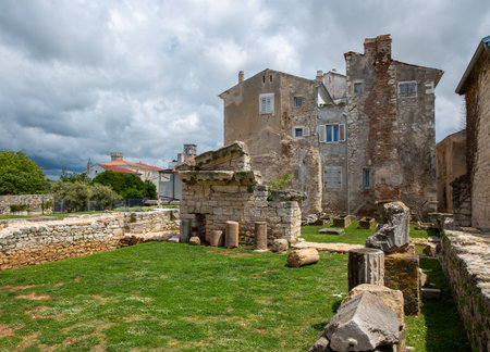 Ancient Roman ruins with broken columns and stone walls in the historic center of Porec, Istria, Croatia. Weathered buildings in the background add to the historical charm.の写真素材