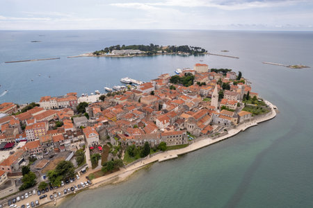 Aerial view of Porec Old Town and the Euphrasian Basilica on the Istrian coast of Croatia. The red-tiled roofs and historical buildings rest along the scenic Adriatic shoreline with nearby marina.の写真素材