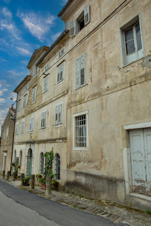 Weathered stone buildings with white wooden shutters line narrow street in medieval hilltop town of Motovun, Istria, showcasing authentic Croatian architecture and old world charm.の写真素材