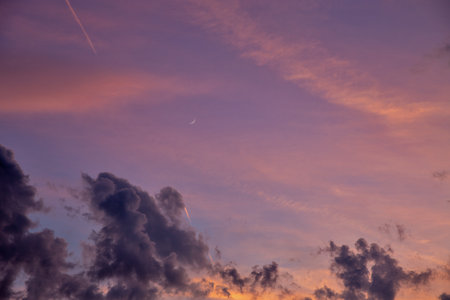 Spectacular purple and pink sunset sky with crescent moon visible through dramatic storm clouds....