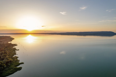Breathtaking sunset over Lake Balaton with vibrant orange and yellow sky reflecting on calm water surface. Perfect golden hour lighting creates stunning Hungarian lakeside landscape scene.の写真素材