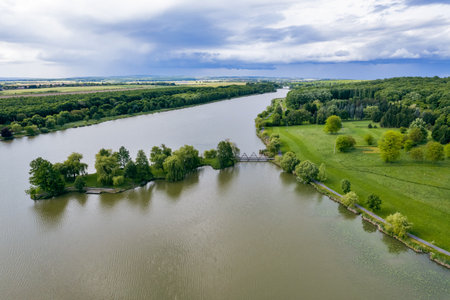 Aerial drone view over serene Boating lake with island in peaceful Hungarian countryside. Lush green vegetation, weeping willows and rural houses create idyllic waterfront landscape.の写真素材